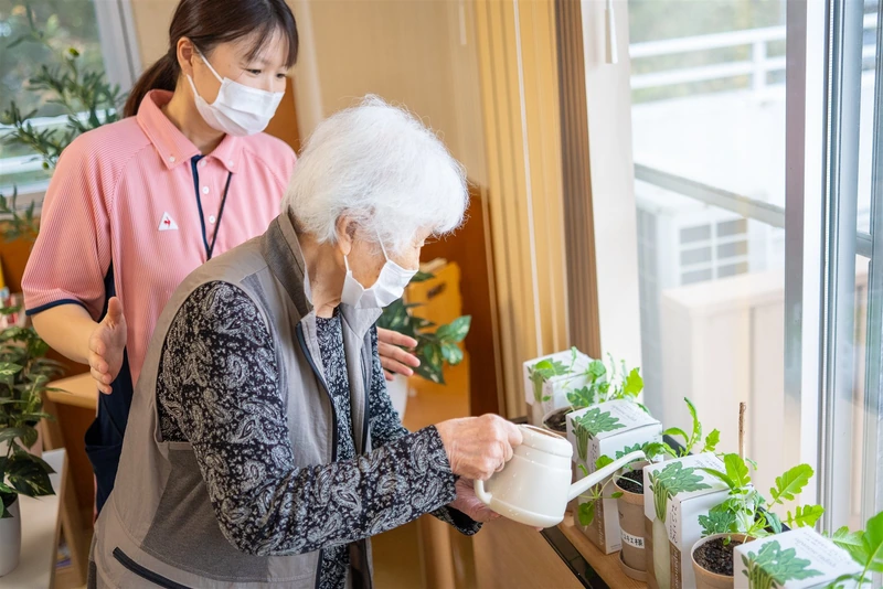 窓辺で植物に水をやる利用者を職員が見守る様子
