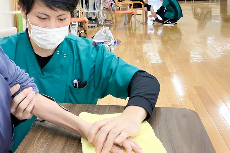 スタッフが利用者の手の動きを支えながら生活動作を練習する様子